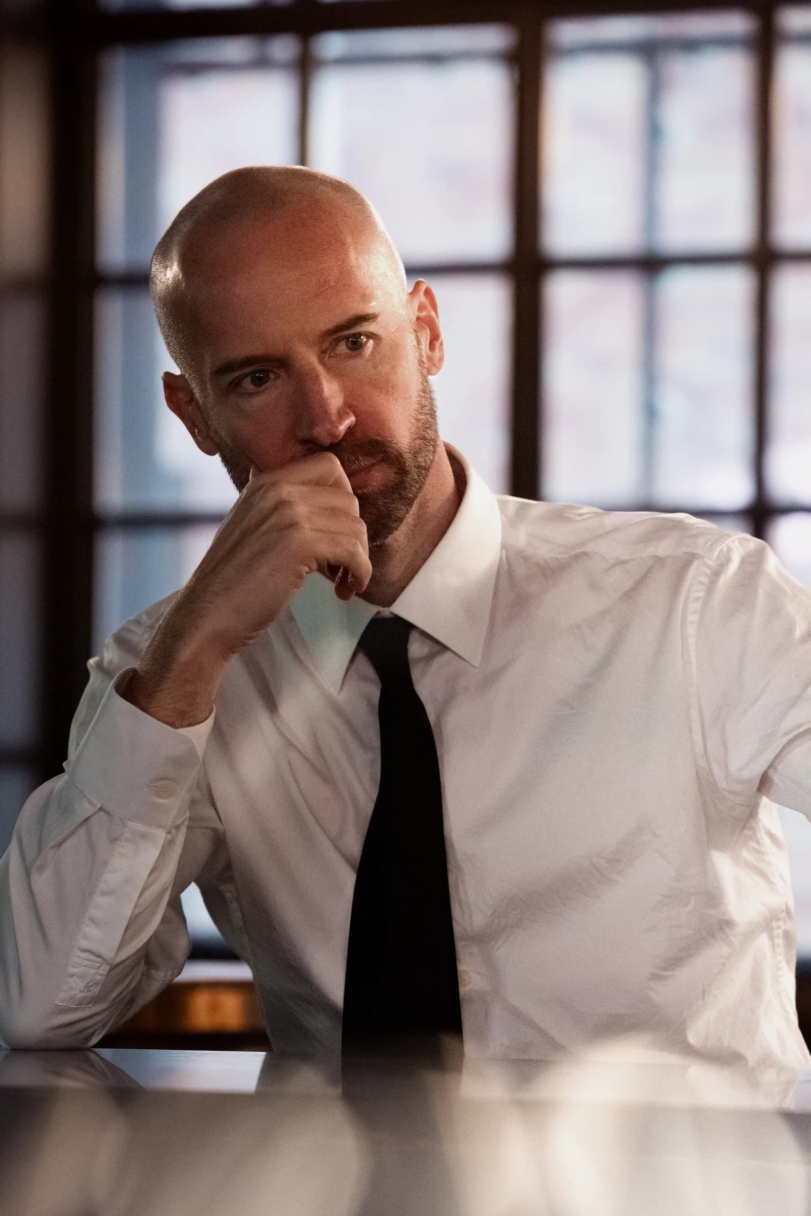 Actor Andreas in a white shirt, resting his face on his hand beside a window.