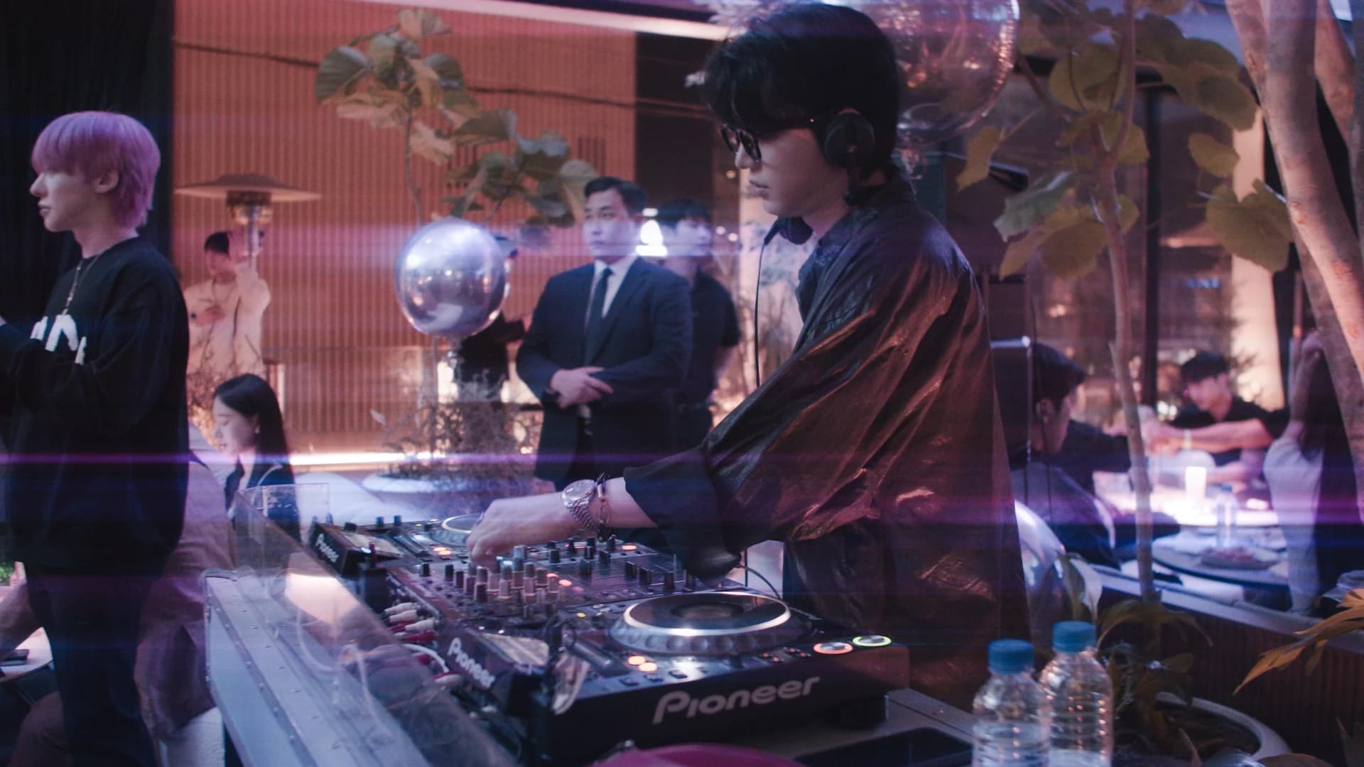 A DJ at the decks in a warm, violet-lit room.