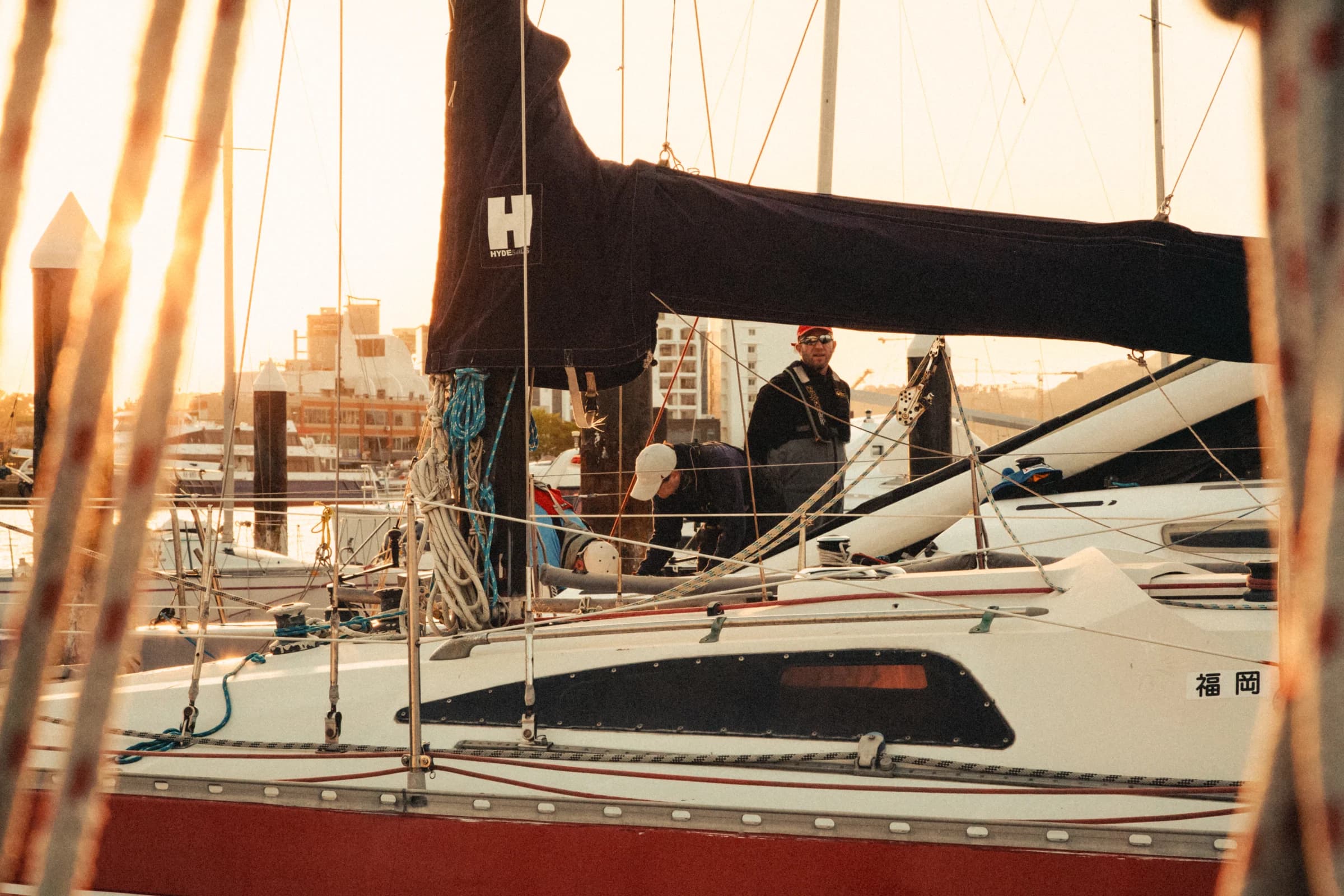 Golden evening light falls across a yacht, its rigging and crew.