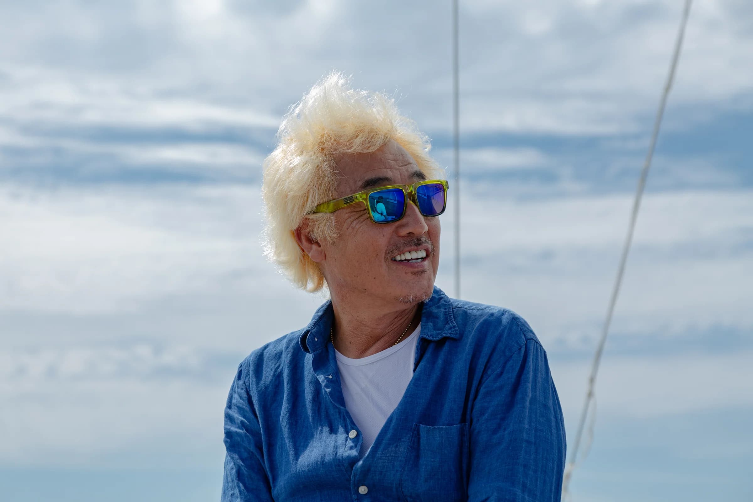 A sailor with windblown blond hair and blue sunglasses aboard a yacht.