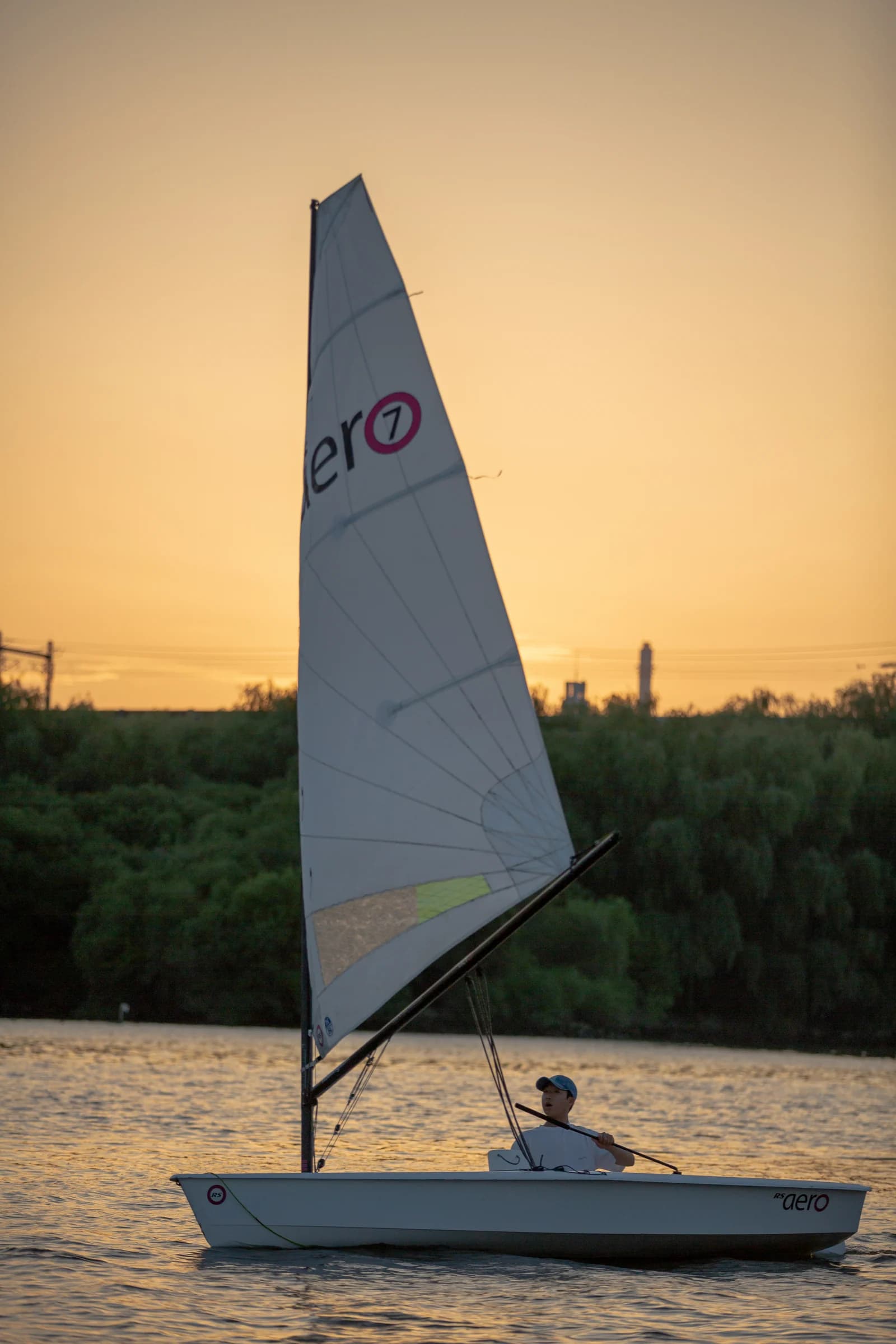 A solitary dinghy sails across golden water at sunset.